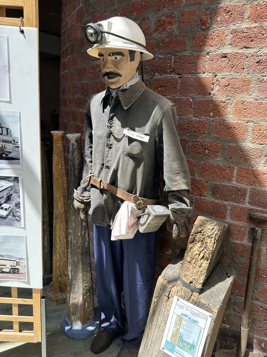 Mannequin en tenue de mineur avec casque et lampe, devant un mur de brique